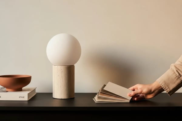 Minimalist shelf with wooden lamp, terracotta bowl, book, and hand holding open magazine